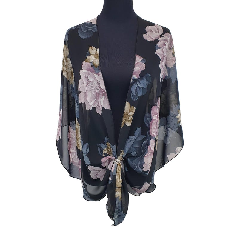 May include: Black floral kimono-style top with a tie front. The sheer fabric features a large-scale floral print in shades of pink, blue, and beige. The top is displayed on a black mannequin.