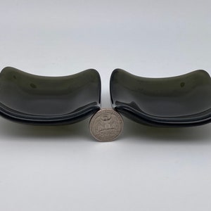 Peut inclure: Deux petits plats en verre gris foncé aux bords arrondis. Les plats sont légèrement incurvés et sont placés côte à côte sur une surface blanche.