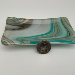 Peut inclure: Un plat rectangulaire en verre avec un motif tourbillonnant de turquoise, de blanc et de marron. Une pièce de monnaie est à côté du plat pour la comparaison de taille. Le plat a une forme légèrement incurvée.