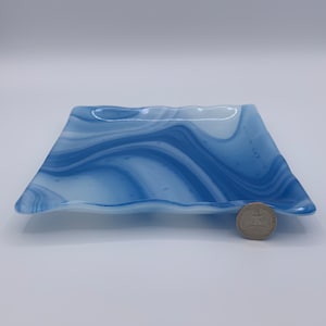 May include: A square, wavy-edged glass dish with a blue and white marbled design. The dish is approximately 15 cm wide and 15 cm long. The colours swirl together, creating a unique pattern. A coin is next to the dish for scale.