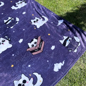 May include: A purple fleece blanket with a repeating pattern of white cats wearing sunglasses. Some cats are in boxes with the text "You Cryin?" and "lol be" on them. Other cats are wearing black jackets and some are floating in the air. The blanket has a white cloud and moon design.