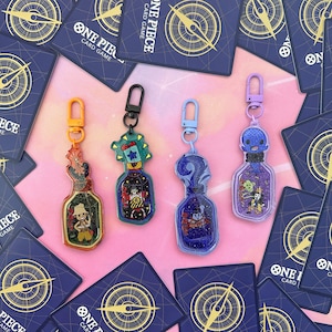 Pu&ograve; includere: Quattro portachiavi colorati con personaggi dell'anime One Piece. Ogni portachiavi &egrave; una bottiglia con un personaggio diverso al suo interno. Le bottiglie sono in acrilico trasparente e hanno un effetto glitter. I portachiavi sono attaccati ad anelli di metallo argentati.