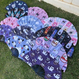 May include: A collection of 10 colourful folding fans with various designs. The fans feature different patterns, including cartoon characters, flowers, and geometric shapes. The fans are made of paper and have a wooden handle.