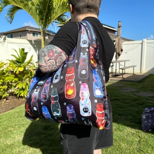 May include: A black reusable tote bag with a colorful print of cartoon characters and Japanese text. The bag is made of a lightweight fabric and has a long strap.