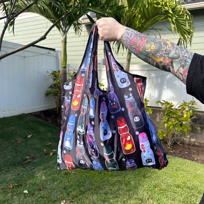 May include: A black reusable tote bag with a colorful pattern of Japanese soda bottles. The bottles have a variety of designs, including a cat, a flower, and a star.