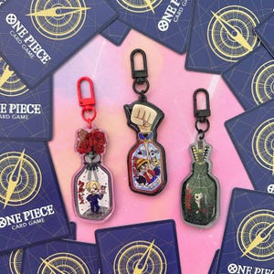 Pu&ograve; includere: Tre ciondoli a forma di bottiglia di vetro trasparente con diversi design. Il primo ciondolo presenta un mazzo di rose rosse, il secondo un pugno con un personaggio dei cartoni animati al suo interno e il terzo un personaggio dei cartoni animati con una spada. Ogni ciondolo ha un anello di metallo nero e una chiusura di metallo argentato.