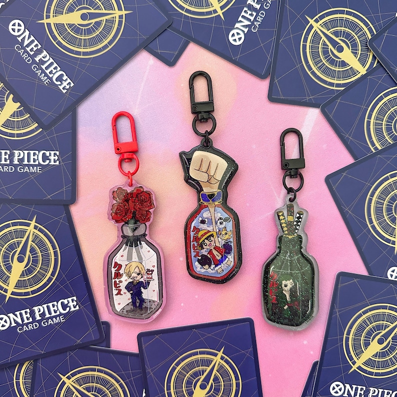 Pu&ograve; includere: Tre ciondoli a forma di bottiglia di vetro trasparente con diversi design. Il primo ciondolo presenta un mazzo di rose rosse, il secondo un pugno con un personaggio dei cartoni animati al suo interno e il terzo un personaggio dei cartoni animati con una spada. Ogni ciondolo ha un anello di metallo nero e una chiusura di metallo argentato.