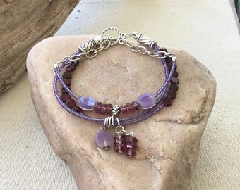 May include: A multi-strand bracelet with purple and garnet beads, silver chain, and a charm with a purple stone.