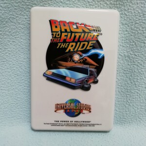 May include: White square-shaped pin with a colorful image of the DeLorean time machine from the Back to the Future movie. The text "Back to the Future the Ride" is above the car. The text "Universal Studios Japan" is below the car.