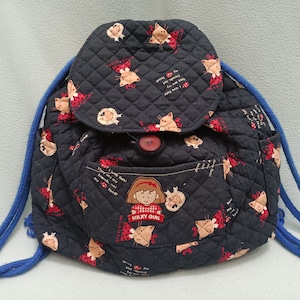 Puede incluir: Una mochila acolchada negra con un cordón de ajuste azul y correas ajustables. La mochila tiene un pequeño bolsillo en la parte delantera con el texto "Milky Girl" y una niña de dibujos animados con un lazo rojo. La mochila está decorada con un patrón repetido de gatos de dibujos animados y mariquitas rojas.