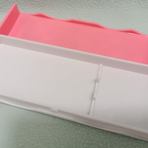 May include: A white plastic storage box with a pink lid. The box has a divider inside to separate items.