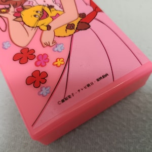 May include: Pink plastic case with a cartoon image of a girl holding a cat. The case has a copyright symbol and the text "&copy; 冒険少女チャレンジャーII・東映動画".