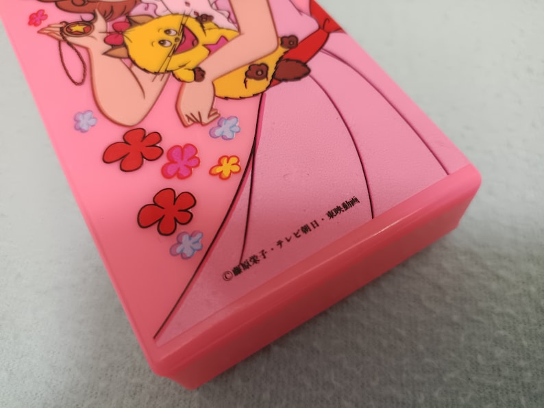 May include: Pink plastic case with a cartoon image of a girl holding a cat. The case has a copyright symbol and the text "&copy; 冒険少女チャレンジャーII・東映動画".