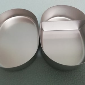 Puede incluir: Dos recipientes de metal ovalados de color plateado con un divisor en uno de los recipientes.