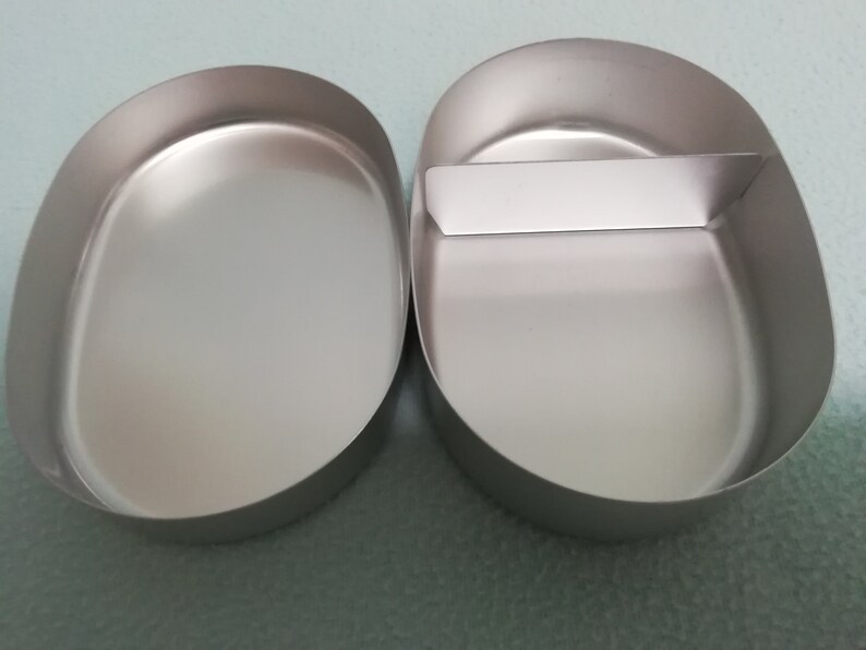 Puede incluir: Dos recipientes de metal ovalados de color plateado con un divisor en uno de los recipientes.