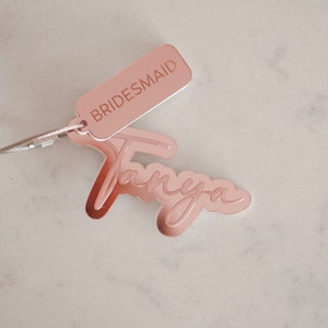 Puede incluir: Llavero de oro rosa con la palabra "BRIDESMAID" y el nombre "Tanya" escrito en cursiva.
