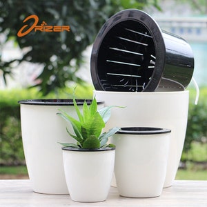 May include: Set of four white plastic self-watering planters with black rims. The largest planter has a black plastic insert with drainage holes. The planters are arranged in a pyramid shape with a small green plant in the smallest planter.