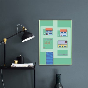 May include: A framed art print with a green background and a pixelated town scene. The artwork features houses, trees, and a blue river. A black desk lamp and decorative bottles are in the foreground.