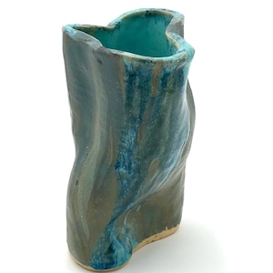 May include: A hand-formed ceramic vase with an irregular, wavy silhouette. The exterior features a blended glaze of muted olive green and deep teal, while the interior is finished in a bright, solid turquoise. The base is unglazed, showing tan clay.