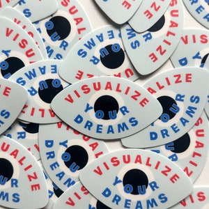 May include: A collection of blue and white eye-shaped stickers with the text "Visualize Your Dreams" in red and blue lettering.
