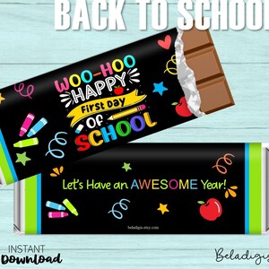 May include: Two chocolate bars with black wrappers. One wrapper says "Woo-Hoo Happy First Day of School" with colorful graphics. The other says "Let's Have an AWESOME Year!" with a red apple and stars. The words "Back to School" are at the top.