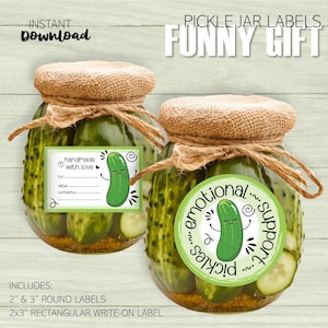 May include: Two glass jars filled with dill pickles, one with a green label that says "handmade with love" and the other with a green circle label that says "emotional support pickles". Both labels feature a cartoon pickle with a smiling face.