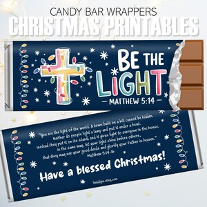 May include: Candy bar wrappers with a Christmas theme. The design features a cross with colorful lights and the words "BE THE LIGHT" with a Bible verse reference. The bottom wrapper says "Have a blessed Christmas!"