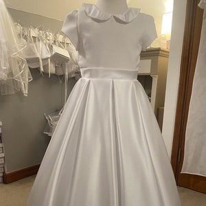 May include: White satin dress with a peter pan collar and short sleeves. The dress has a full skirt and is perfect for a special occasion.