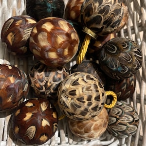 May include: A collection of decorative spheres made from pheasant feathers in various patterns and colours, including brown, black, and teal. The spheres are arranged in a white wicker basket.