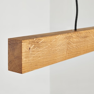 May include: A wooden pendant light fixture with a natural wood finish. The light fixture is suspended from a black wire.