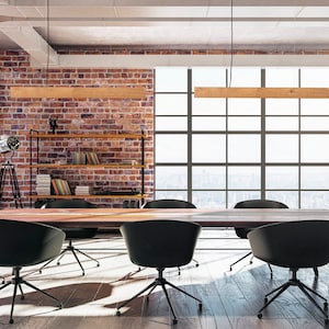 May include: A long wooden table with black chairs sits in a modern office space with exposed brick walls and large windows. The room has a minimalist design with a bookshelf and a tripod lamp.
