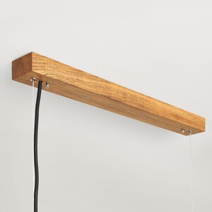 May include: A wooden ceiling mount with two black wires hanging down. The mount is made of natural wood and has a rectangular shape.