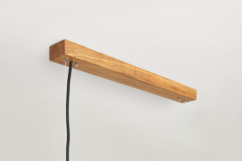 May include: A wooden ceiling mount with two black wires hanging down. The mount is made of natural wood and has a rectangular shape.