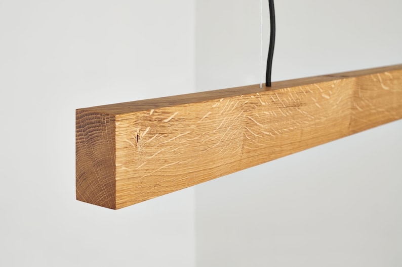 May include: A wooden pendant light fixture with a natural wood finish. The light fixture is suspended from a black wire.