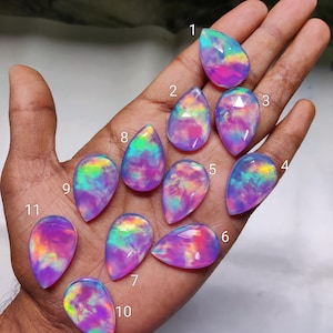 May include: A collection of eleven teardrop-shaped opals, each displaying a unique play of color. The opals showcase a vibrant mix of pink, purple, blue, and green hues, with a polished, glossy finish. The gemstones are arranged on a hand.