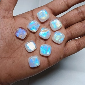 Peut inclure: Une collection de neuf cabochons de pierre de lune iris&eacute;s dans diff&eacute;rentes nuances de blanc et de bleu. Les pierres sont taill&eacute;es en forme carr&eacute;e et ont une finition lisse et polie.