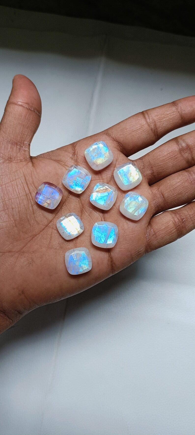 Peut inclure: Une collection de neuf cabochons de pierre de lune iris&eacute;s dans diff&eacute;rentes nuances de blanc et de bleu. Les pierres sont taill&eacute;es en forme carr&eacute;e et ont une finition lisse et polie.