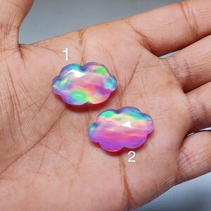 May include: Two iridescent pink and purple cloud-shaped cabochons with a rainbow sheen. The cabochons are labeled 1 and 2.
