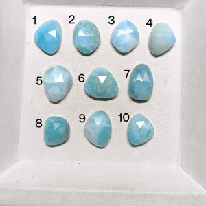 May include: Ten light blue, iridescent, cabochon gemstones arranged in rows on a white surface. Each gemstone is numbered 1 through 10.