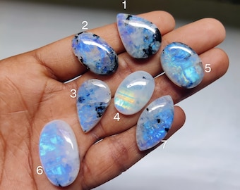 May include: Seven iridescent moonstone cabochons in various shapes and sizes, including oval, teardrop, and pear. The stones have a milky white base with blue and green iridescence.