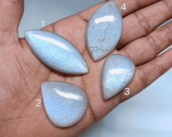 May include: Four iridescent, pearlescent, white, and gray gemstone cabochons in various shapes, including oval, teardrop, and pear, on a hand.