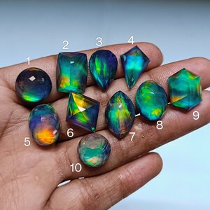 Puede incluir: Diez piedras preciosas iridiscentes de diversas formas y tamaños, incluyendo redondas, ovaladas, en forma de pera y cuadradas, con un arcoíris de colores, incluyendo verde, azul y morado.