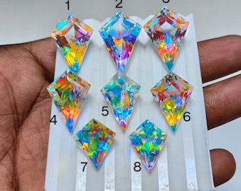 May include: Eight iridescent, faceted, clear glass stones with rainbow colors. The stones are arranged in rows on a white surface.