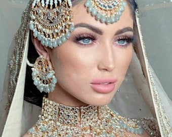 May include: A woman wearing a traditional Indian bridal outfit with a white veil and a silver and gold headpiece with pearls. She is also wearing a silver and gold necklace with pearls and a matching pair of earrings.