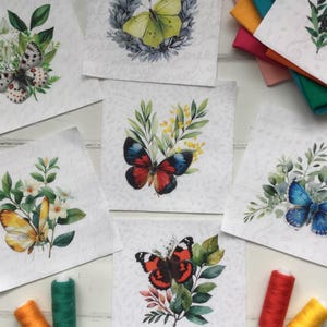 Może przedstawiać: Kolekcja kwadratowych naszywek z tkaniny z akwarelowymi ilustracjami motyli. Każda naszywka przedstawia inny gatunek motyla w żywych kolorach, otoczony elementami kwiatowymi. Widoczne są również szpulki nici w różnych kolorach.