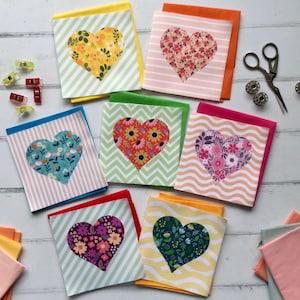 May include: Eight handmade cards featuring a variety of colourful floral heart designs. The cards are all different sizes and shapes, and they are all made with a white background.