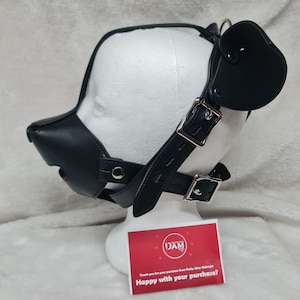 May include: Black leather dog muzzle with a strap and a black leather ear piece. The muzzle is on a white mannequin head. The text on the card reads "Happy with your purchase?"