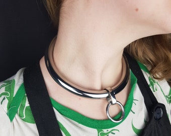 May include: A silver metal choker necklace with a round ring attached. The necklace is worn by a person with blonde hair.