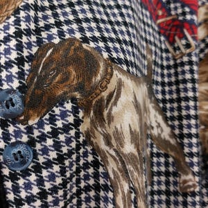 Può includere: Primo piano di un tessuto a pied-de-poule blu e bianco con un'illustrazione di un cane marrone e bianco. Il cane indossa un collare di cuoio marrone. Il tessuto ha due bottoni blu con la parola "Smock" su di essi.