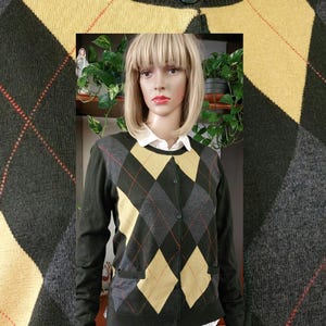 Peut inclure: Un cardigan en argyle vert, gris et jaune avec une fermeture boutonnée. Le cardigan a une poche sur le côté gauche.